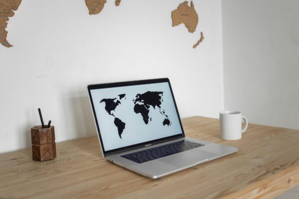 A minimalist desk setup with a laptop showing a world map screen and a mug, set against a wall map backdrop.